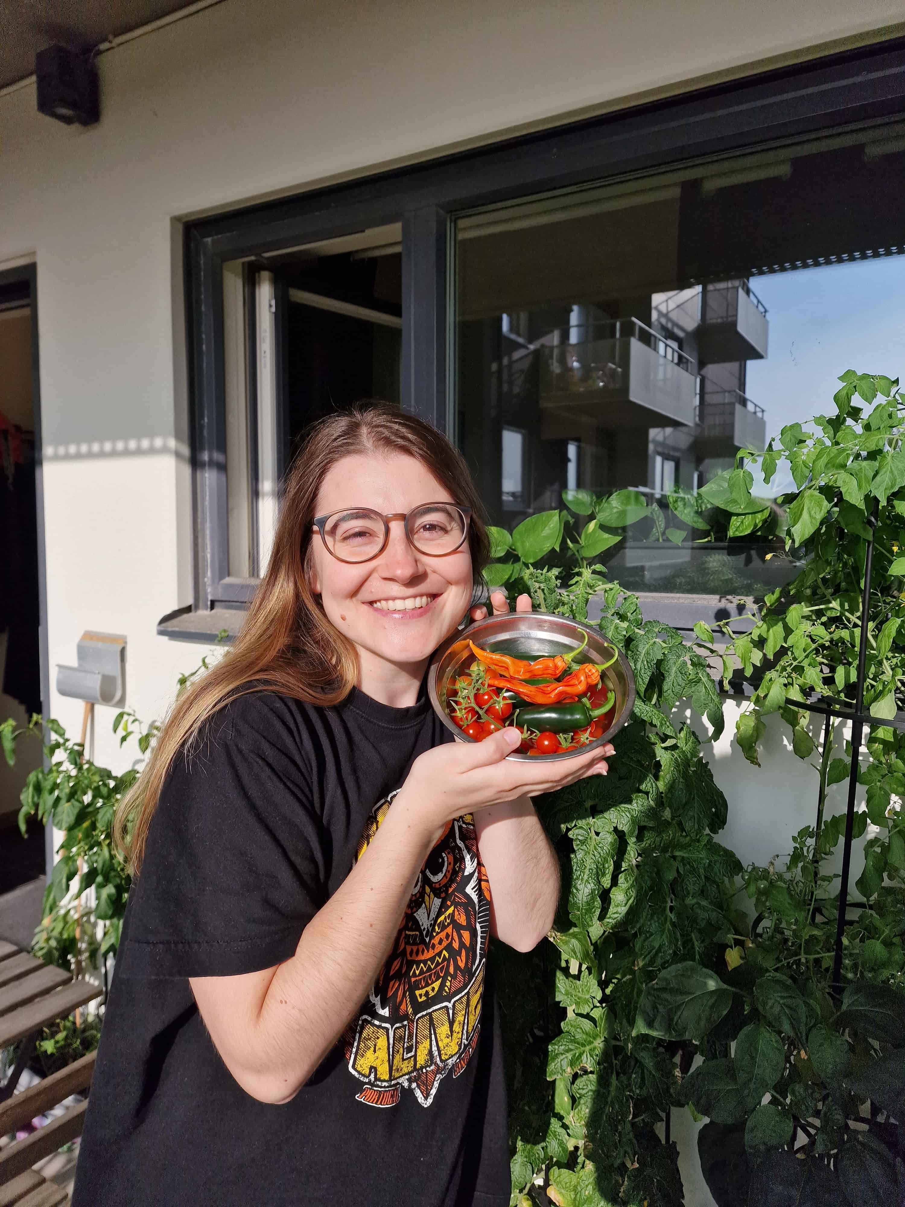 Portrait in the balcony surrounded by thriving plants and holding part of yield for that season